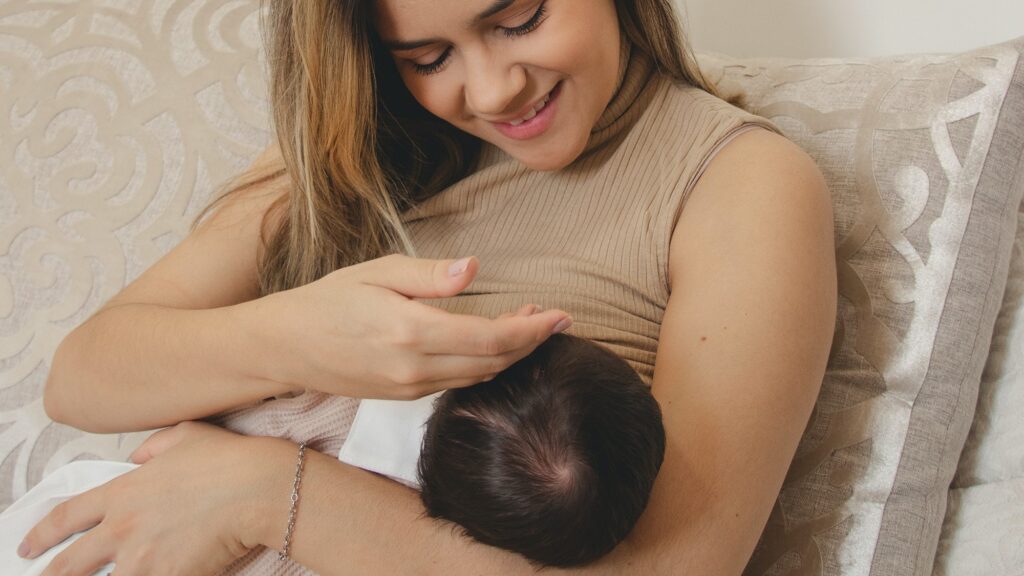 A smiling mother sitting on a couch breastfeeding her baby