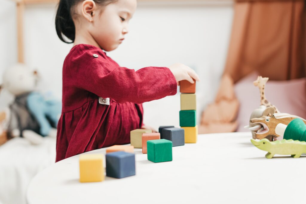 Little girl in a red dress playing with square wooden blocks of different colours