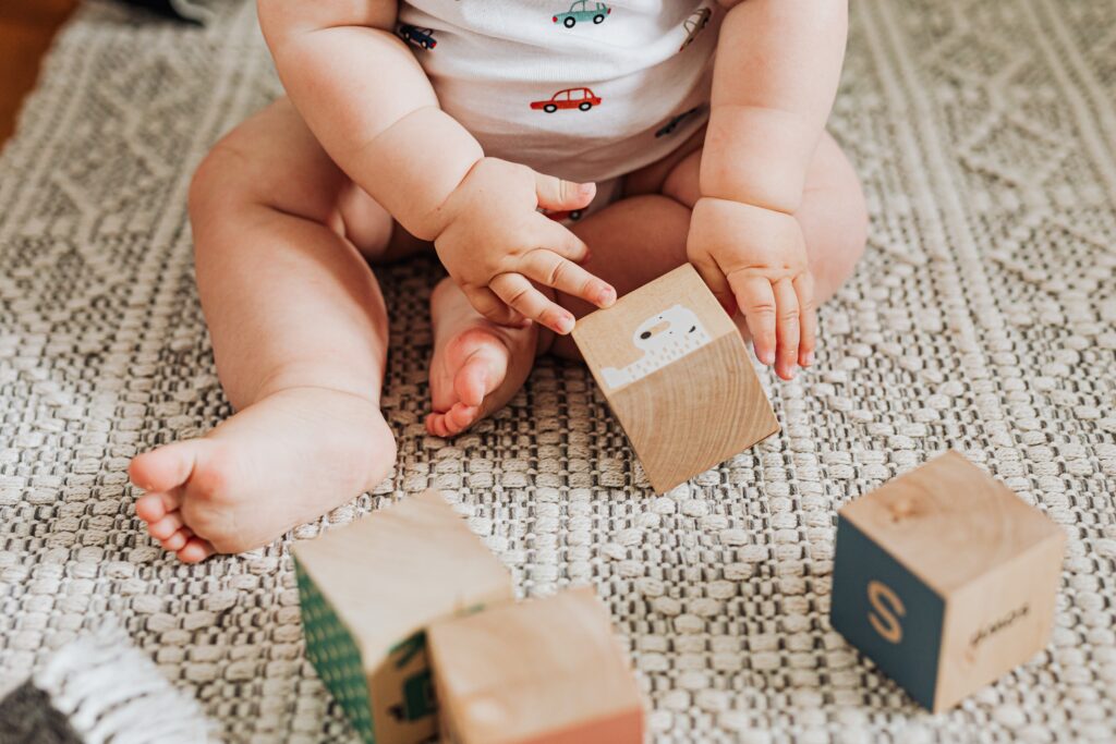 Baby sitting on the floor playing with Wooden Block Developmental Toy
