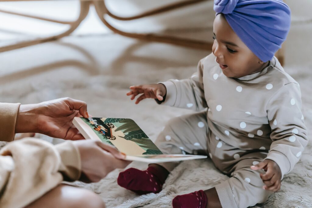 A baby sitting on a rug looking at and Interacting with a Sensory Book
